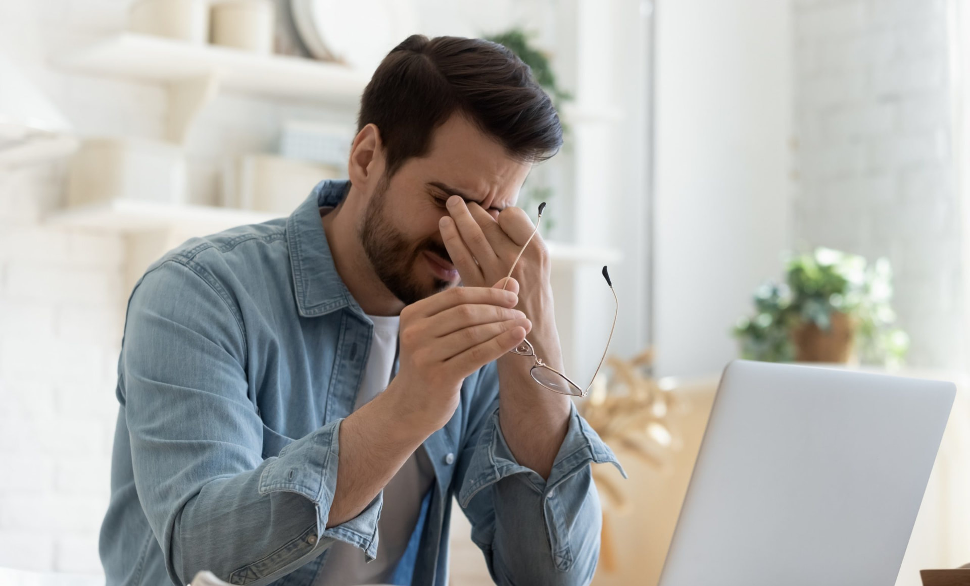 Stressad man vid dator som tar av sig glasögonen
